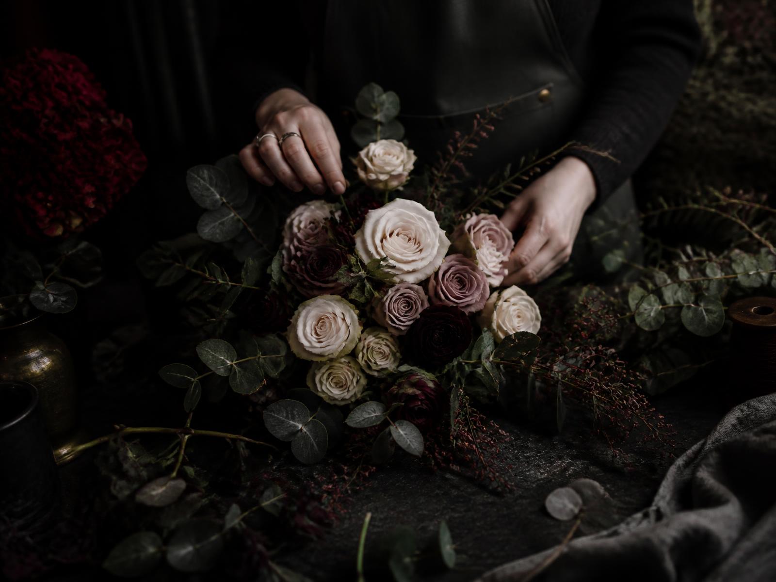 Florist arranging pale roses on a dark workbench
